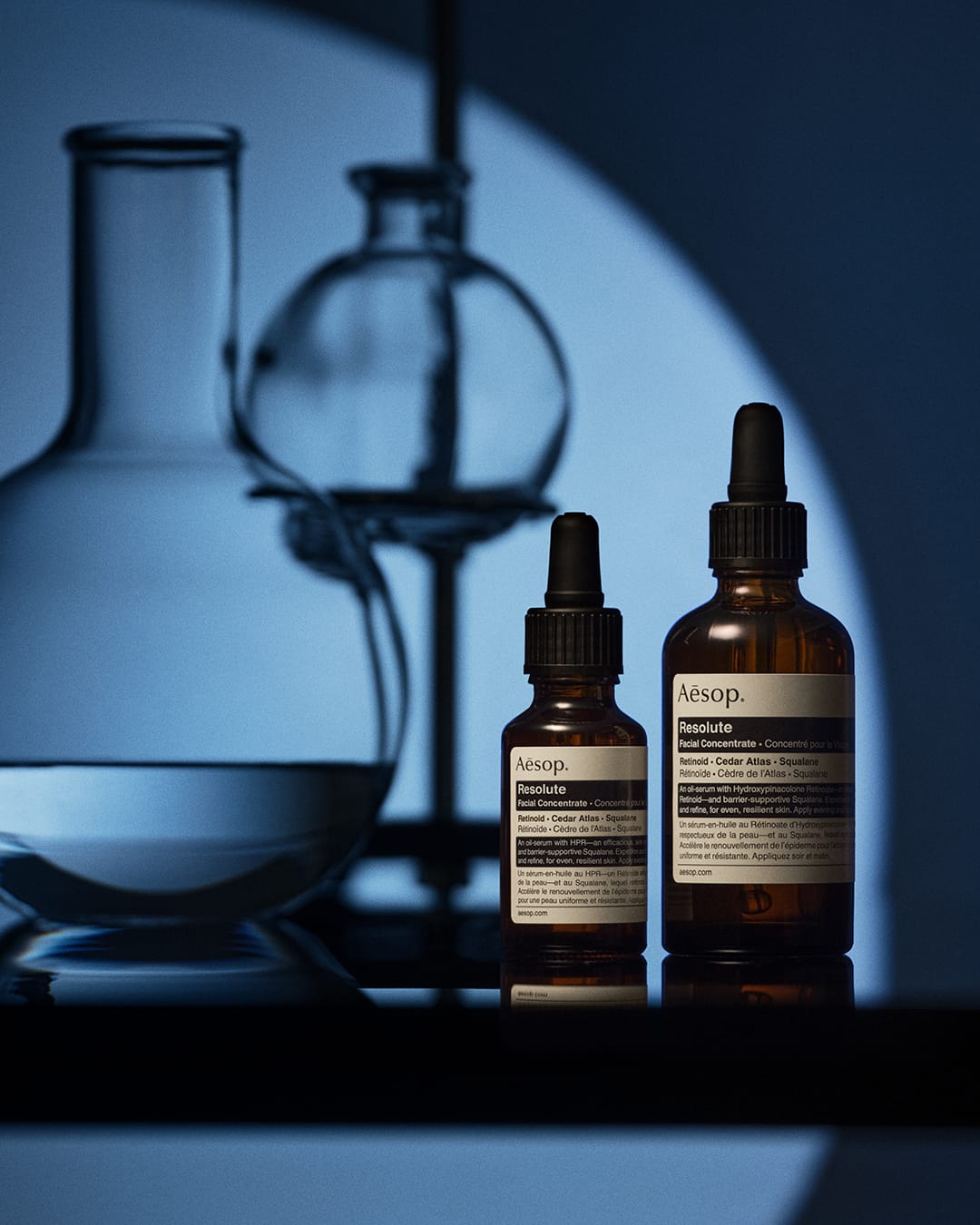 Aesop skincare product photo: deep blue, amber brown and black, glass, dramatic light