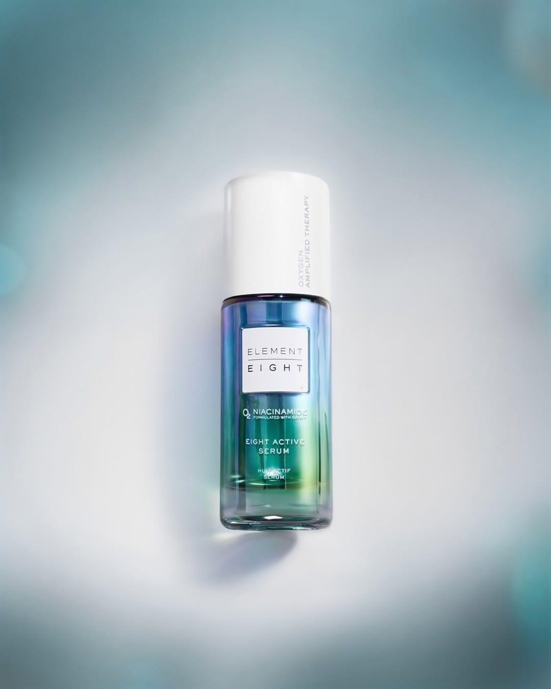 Element Eight serum product photo: white cap, ocean blue and teal green, glass, soft light