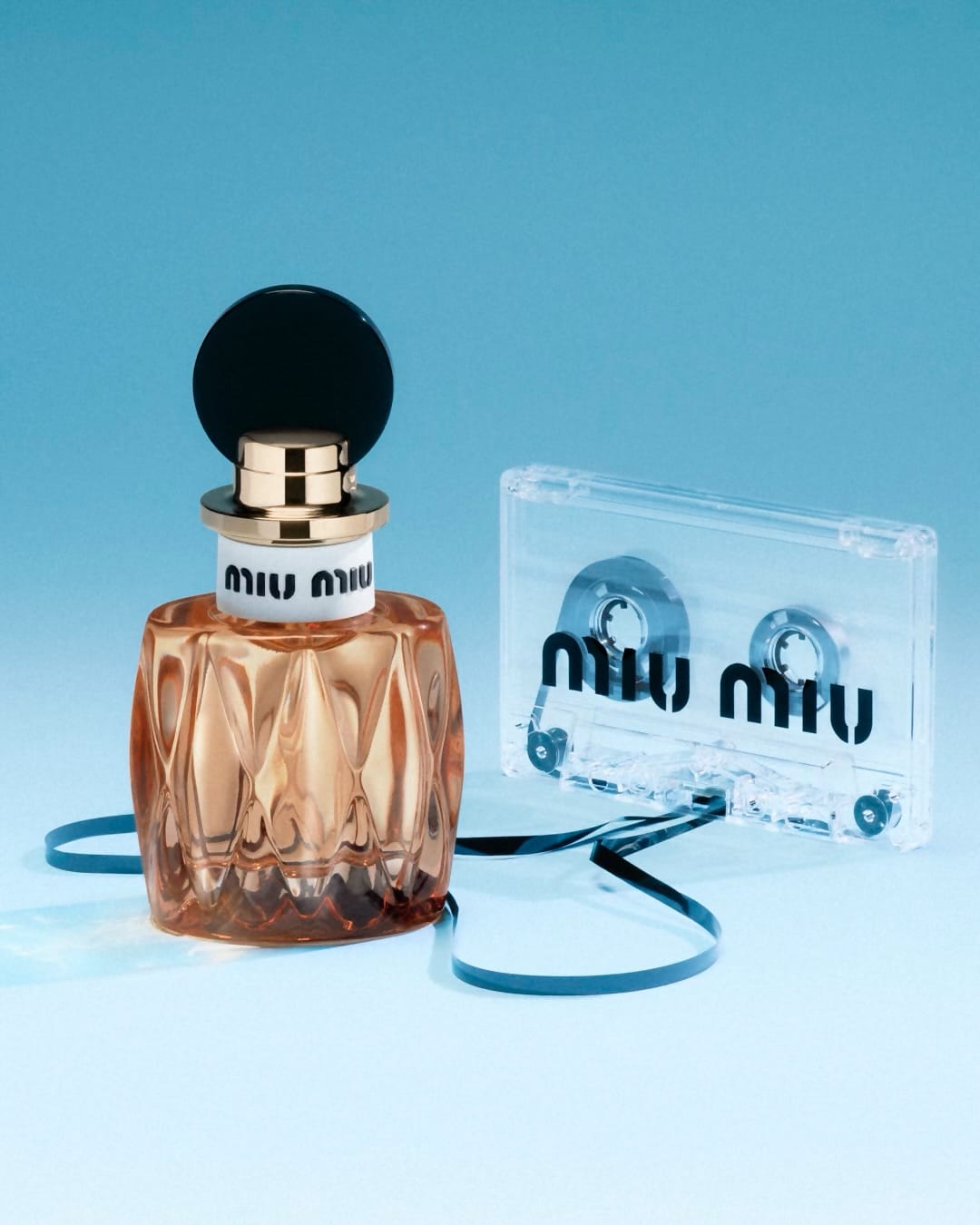 Miu Miu fragrance product photo: aqua blue, peach amber, black cap and gold, glass, soft light, image 3 of 3